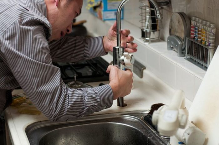Encanador prestando assistência residencial, consertando torneira de pia da cozinha
