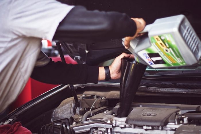 Capô aberto de veículo e um mecânico segurando funil e frasco de óleo de motor, colocando óleo para evitar superaquecimento do motor