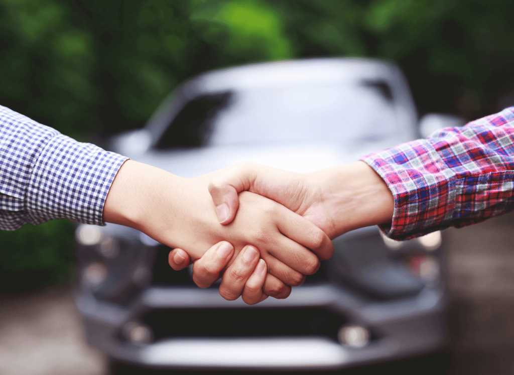 duas pessoas apertando as mãos em frente a um carro